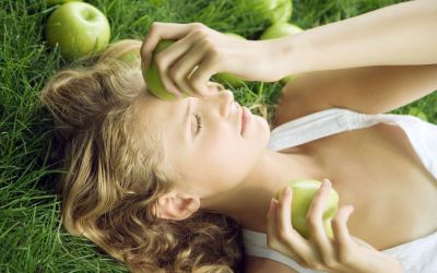 Woman lying in grass, holding apple to forehead
